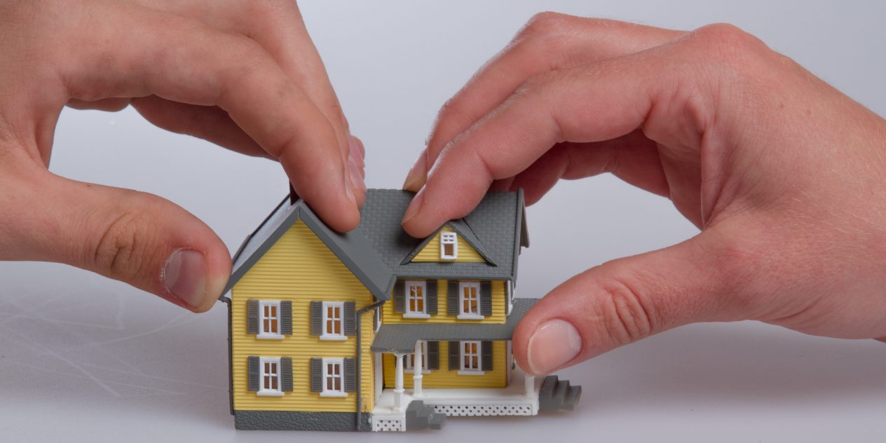 Human Hands Holding a Model of a House as they separate over divorce